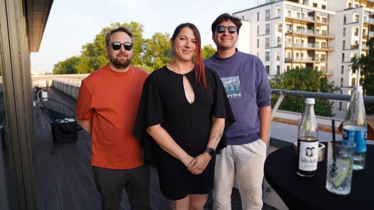 Three colleagues on the office roof terrace in the evening sun, at the start of the summer party