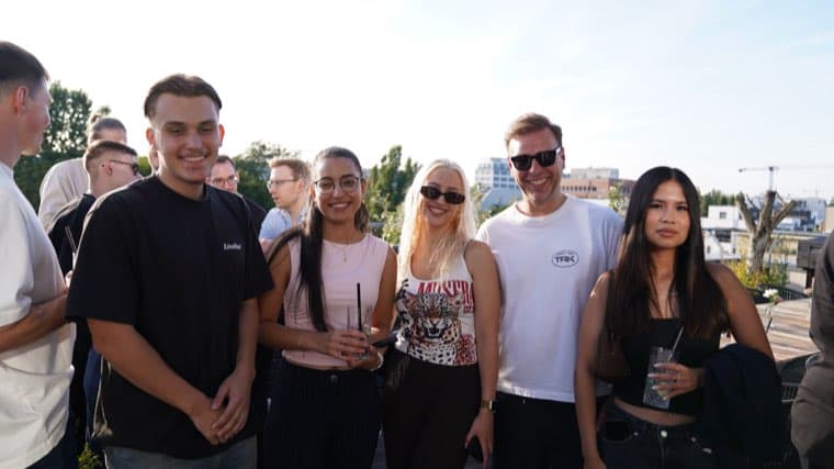 Six colleagues outdoors on the terrace in low evening sun, drinks in hand