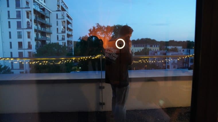 A colleague standing at the terrace railing at dusk, seen through the glass with the street lights beyond