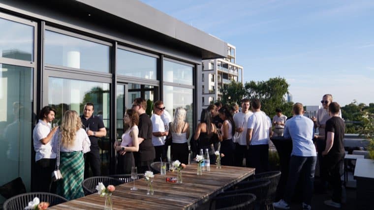 The roof terrace seen from its far end, the office window wall on the left and colleagues standing along it