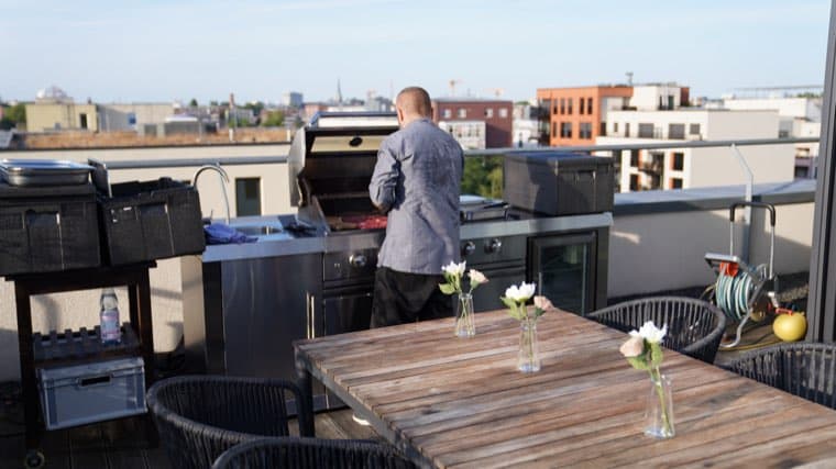 A colleague working the grill on the roof terrace, city rooftops behind him