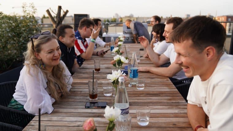 Colleagues laughing at the terrace table in the evening, the skyline behind the railing